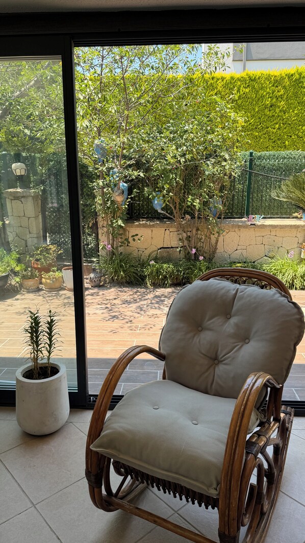 A wicker chair with a cushioned seat and back, positioned in front of a large window with a view of a garden.