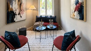 Een moderne woonkamer met een bank, twee stoelen, een vloerkleed en abstracte schilderijen aan de wanden.