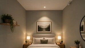 Een slaapkamer met een bed, nachtlampjes, een nachtkastje, een dressoir, een spiegel, een wandplank met een plant, en een lijst met een afbeelding boven het bed.
