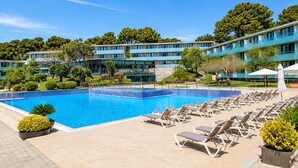 A swimming pool with lounge chairs, a building with multiple floors, and surrounding greenery. - Romantic Coastal Apartment Hideaway (Castell-Platja d'Aro)