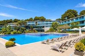 A swimming pool with lounge chairs, a building with multiple floors, and surrounding greenery. - Romantic Coastal Apartment Hideaway (Castell-Platja d'Aro)