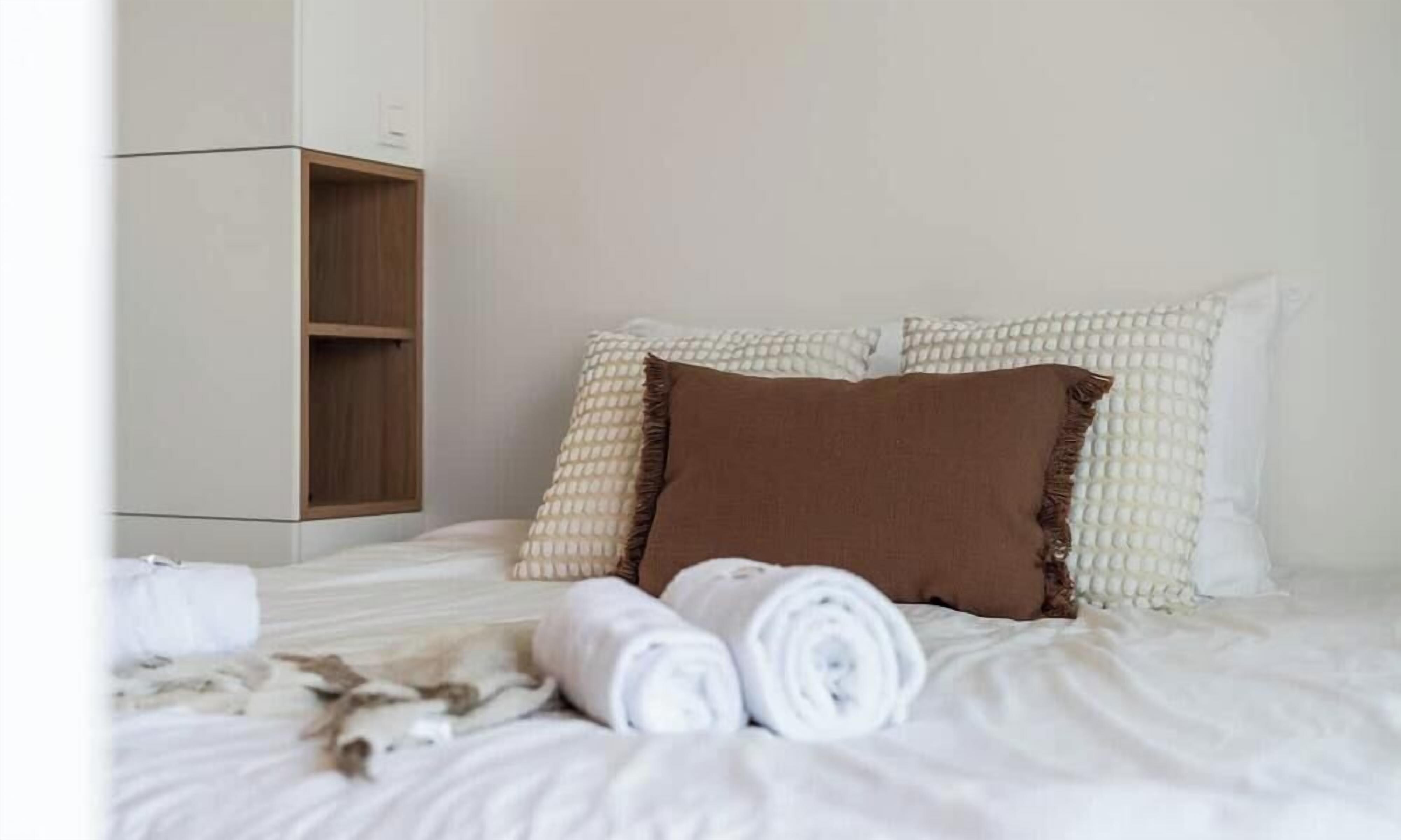 Una habitación de hotel con cama, almohadas, un armario de madera y toallas enrolladas.