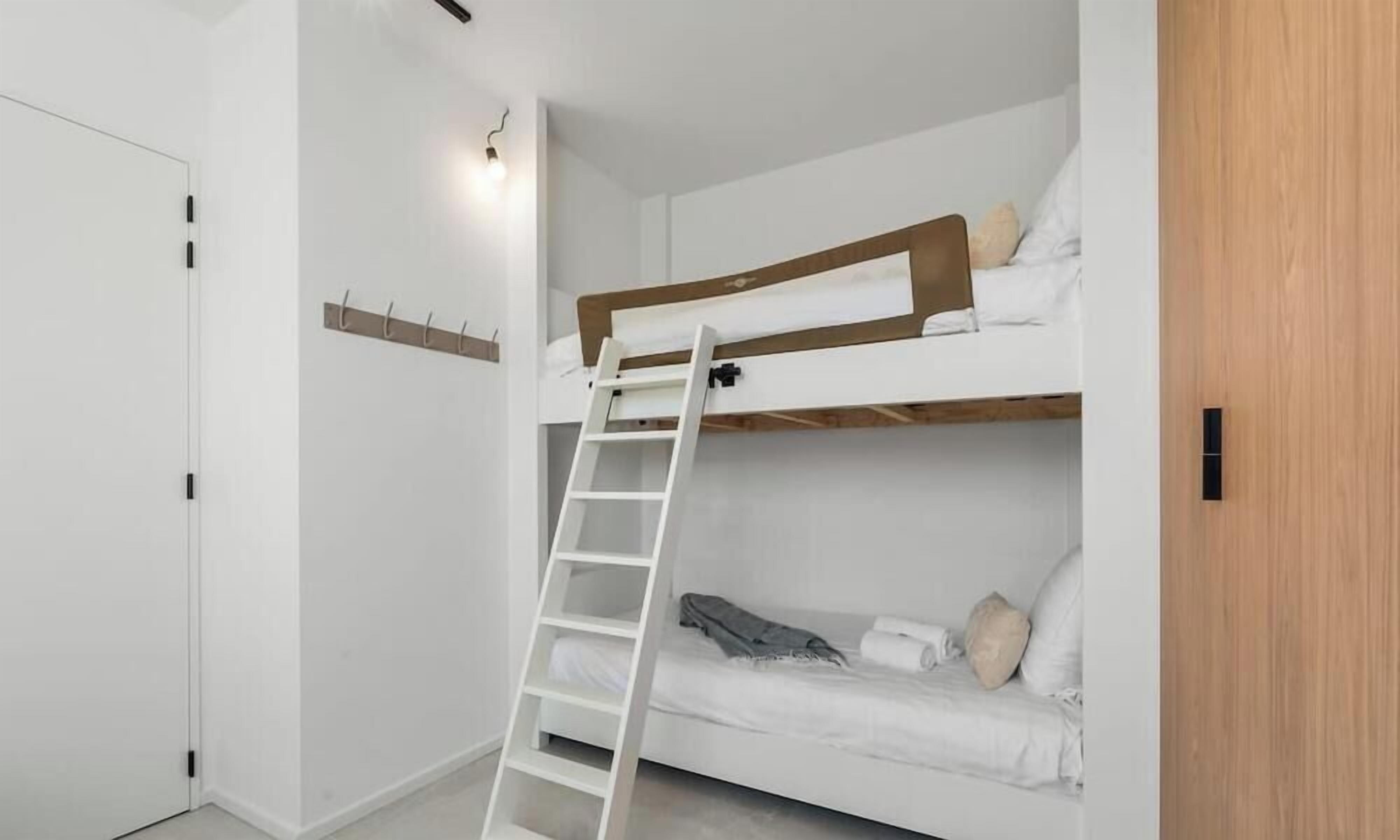 Une chambre avec un lit superposé, une échelle, des murs blancs et une porte en bois.