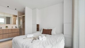 Ein modernes Schlafzimmer mit einem Bett, einem Holzschrank, einem Spiegel und einem durchgehenden Türspalt erkennbaren Badezimmer.