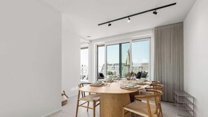 Ein moderner Essbereich mit einem runden Holztisch, sechs Stühlen und einem großen Fenster mit Blick auf die Stadt.