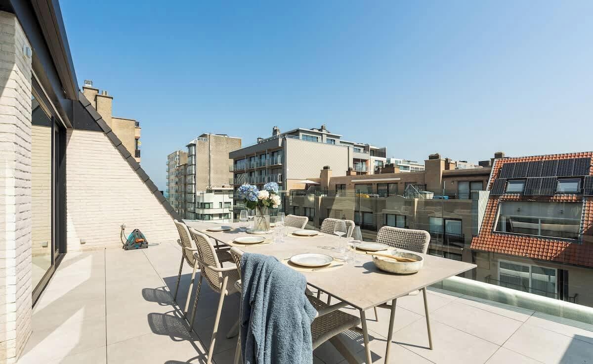 Terrassa al terrat amb taula de dinar per a quatre persones, amb cadires de vimetla i vista despejada cap a l'horitzó urbà.