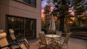 Eine Terrasse im Freien mit Tisch und Stühlen, einem Grill und Blick auf Bäume und einen Sonnenuntergang.