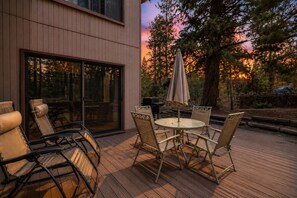 An outdoor deck with a table and chairs, a grill, and a view of trees and a sunset. - 4BR/3BA Big Bear Lake Retreat w/ Forest View (Big Bear Lake)