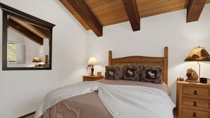 Ein Schlafzimmer mit einem Holzkopfteil, einem großen Bett mit einer beigen Tagesdecke, zwei Nachttischen mit Lampen, einem Spiegel und einer Kommode mit Schubladen.