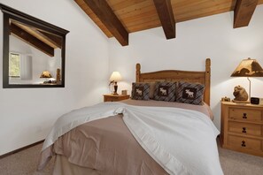 A bedroom with a wooden headboard, a large bed with a beige bedspread, two bedside tables with lamps, a mirror, and a dresser with drawers. - 4BR/3BA Big Bear Lake Retreat w/ Forest View (Big Bear Lake)