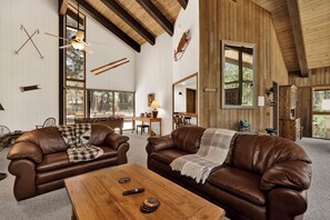 Un salon spacieux, doté de canapés en cuir, d’une table basse en bois et de grandes fenêtres offrant une vue sur l’extérieur.