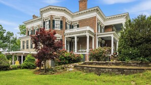 A large, two-story house with a wrap-around porch, brick exterior, and a well-maintained garden.