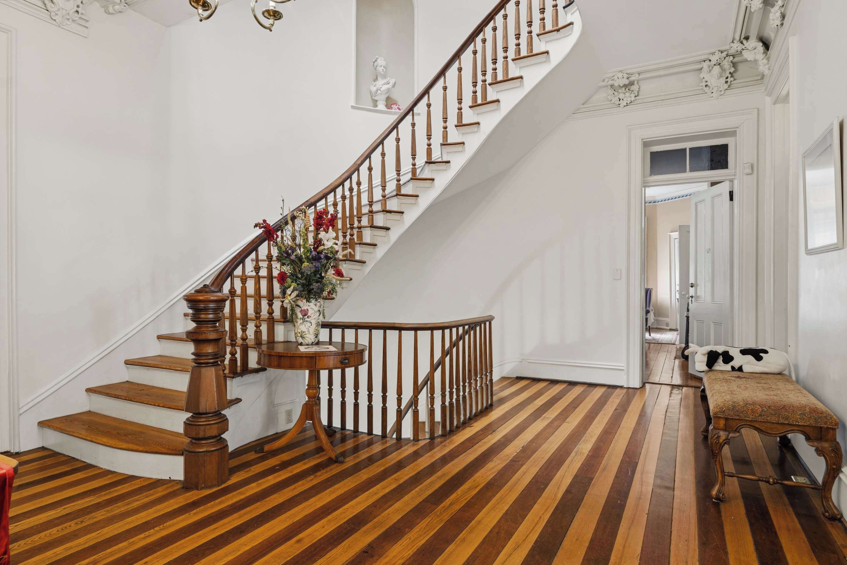 A staircase with wooden steps and a railing, a bench, and a vase with flowers.