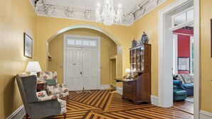 A room with a patterned wooden floor, a floral armchair, a wooden cabinet, and a chandelier.