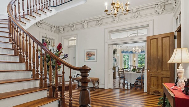 A grand staircase with wooden balusters, a chandelier, and a dining area with a table and chairs.