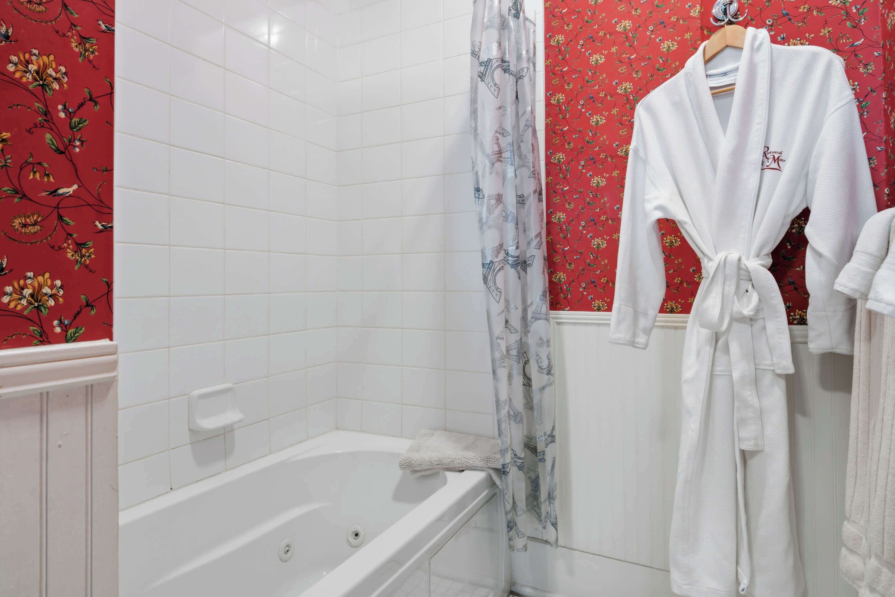 Een badkamer met een witte badkuip, een douchegordijn met bloemenprint en een witte badjas aan een rek.