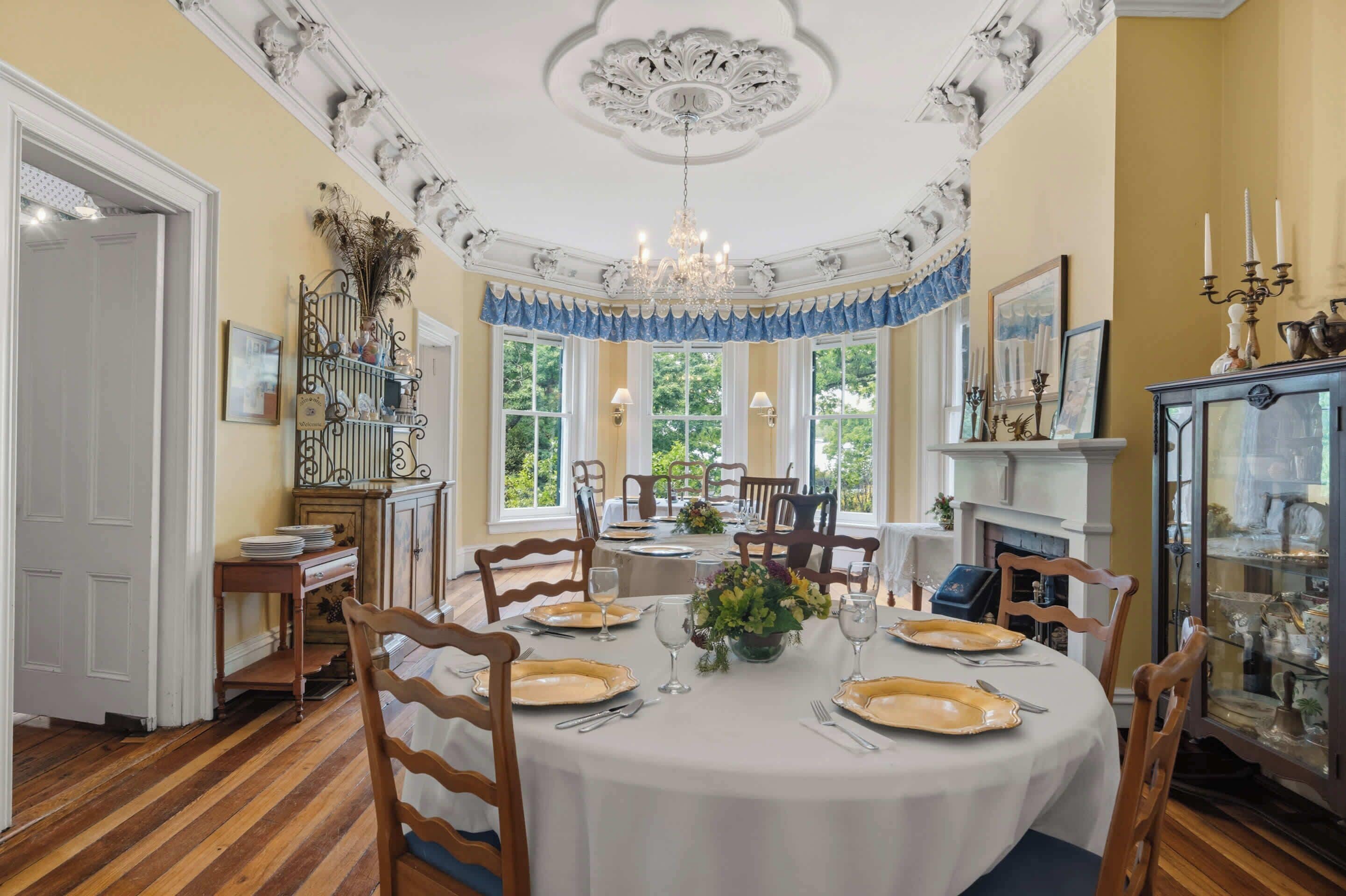 A dining room with a round table set for six, surrounded by wooden chairs.