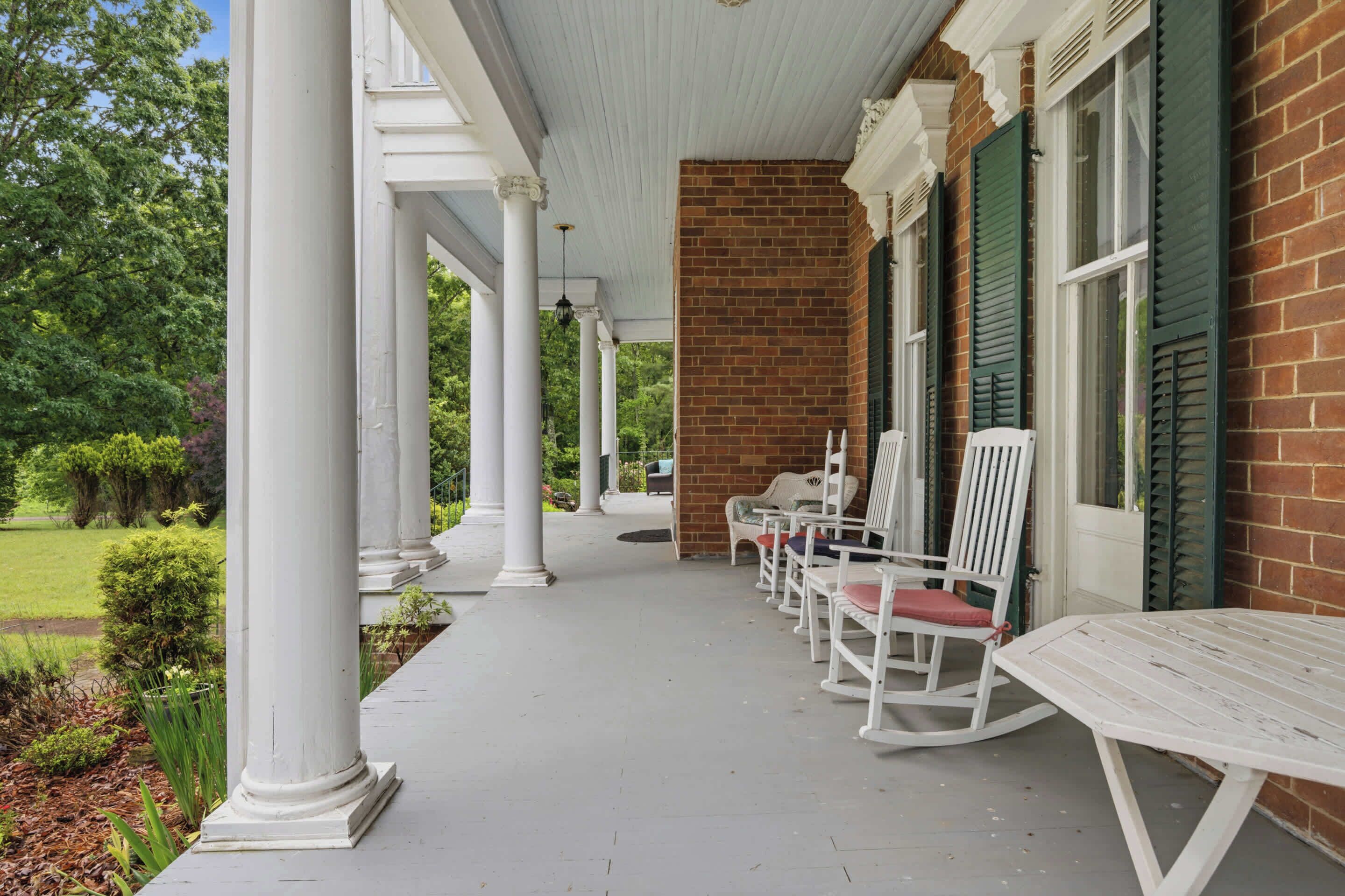 A covered porch with white columns, a brick wall, and a row of white rocking chairs.