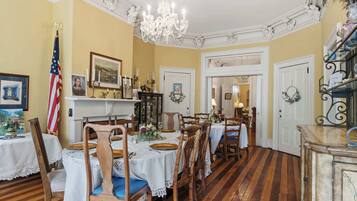 A dining room with a wooden floor, white walls, and a chandelier.