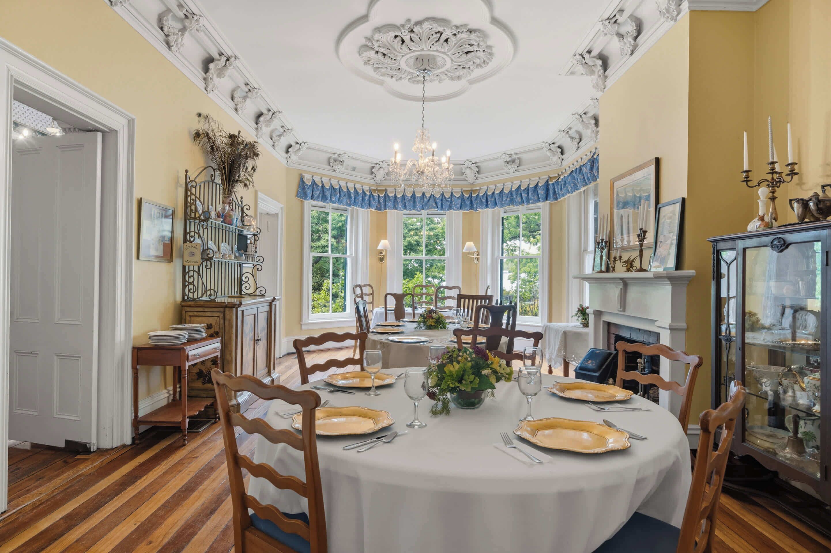 A dining room with a round table set for six, surrounded by wooden chairs.