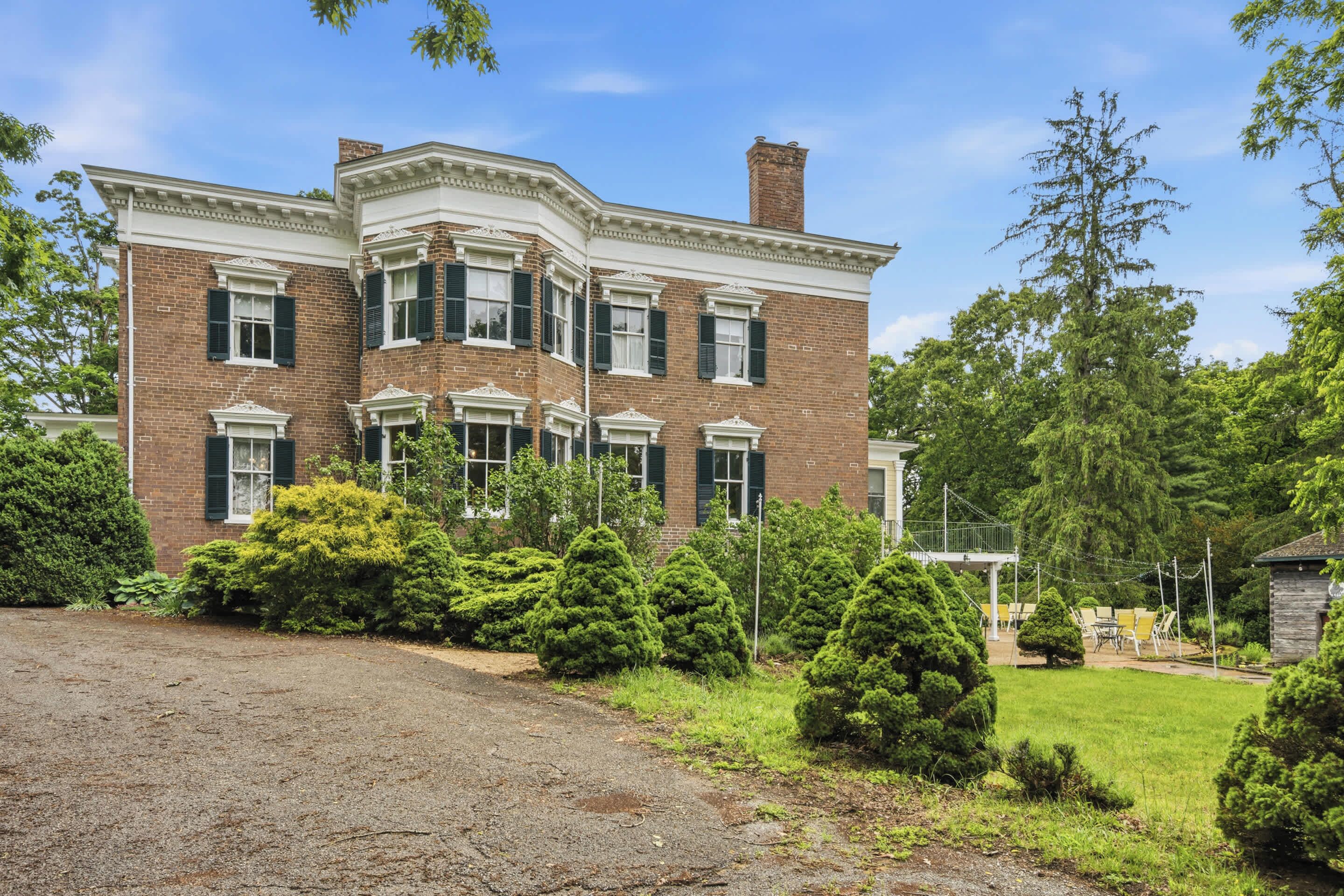 A large brick building with a symmetrical facade, multiple windows, and a well-maintained lawn with various shrubs.