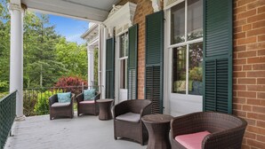 A covered porch with wicker furniture and green shutters.