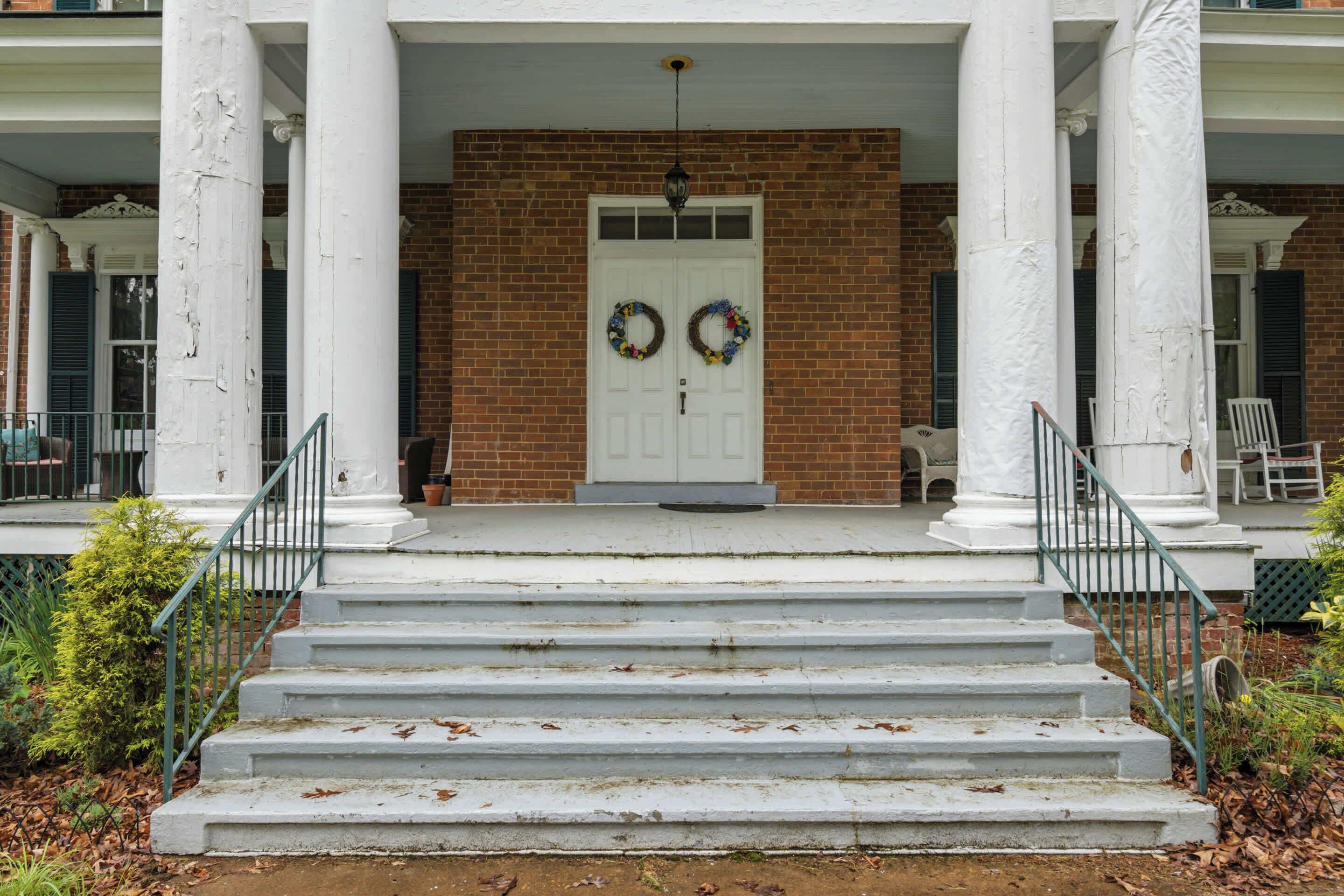 A front porch with a white door, two wreaths, and a brick wall.