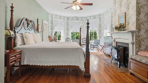 A bedroom with a four-poster bed, a fireplace, and a view of the outdoors.