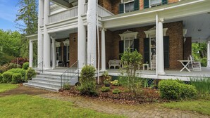 A two-story brick house with a porch, white columns, and green shutters.