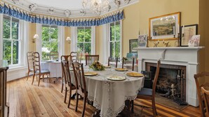 A dining room with a round table, chairs, a fireplace, and framed pictures on the wall.