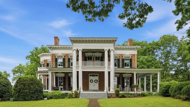 A two-story brick house with a central porch, a front door with a wreath, and a well-maintained lawn.
