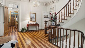 A grand staircase with a wooden handrail, a chandelier, and a floral arrangement on the landing.