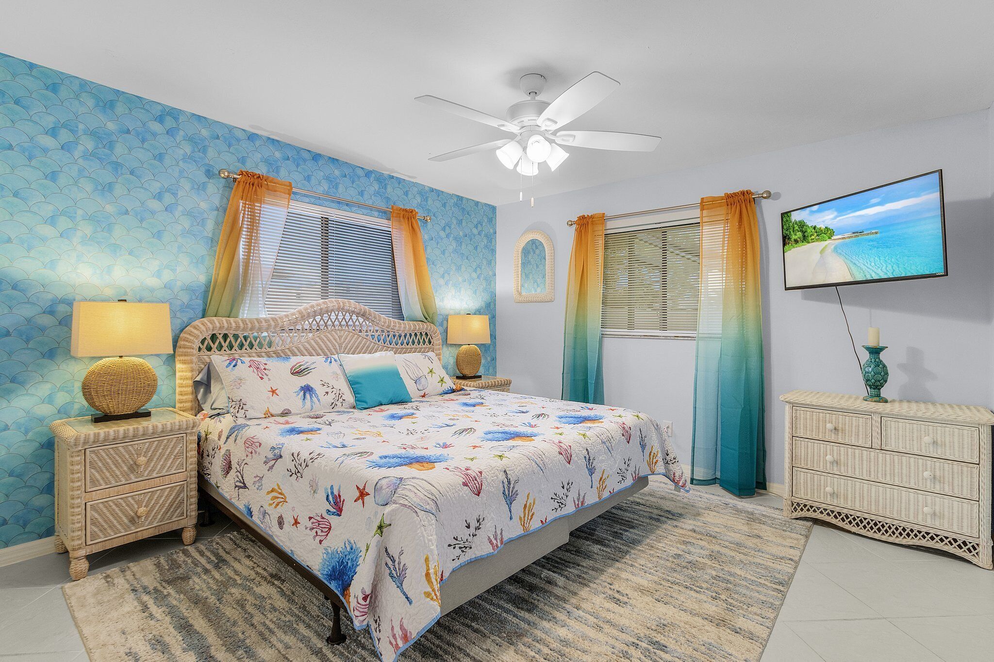 Une chambre à coucher comprenant un lit, des tables de chevet, une commode, un ventilateur de plafond et un téléviseur fixé au mur.
