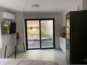 A modern apartment with a balcony, a TV mounted on the wall, a refrigerator, and a glass table.