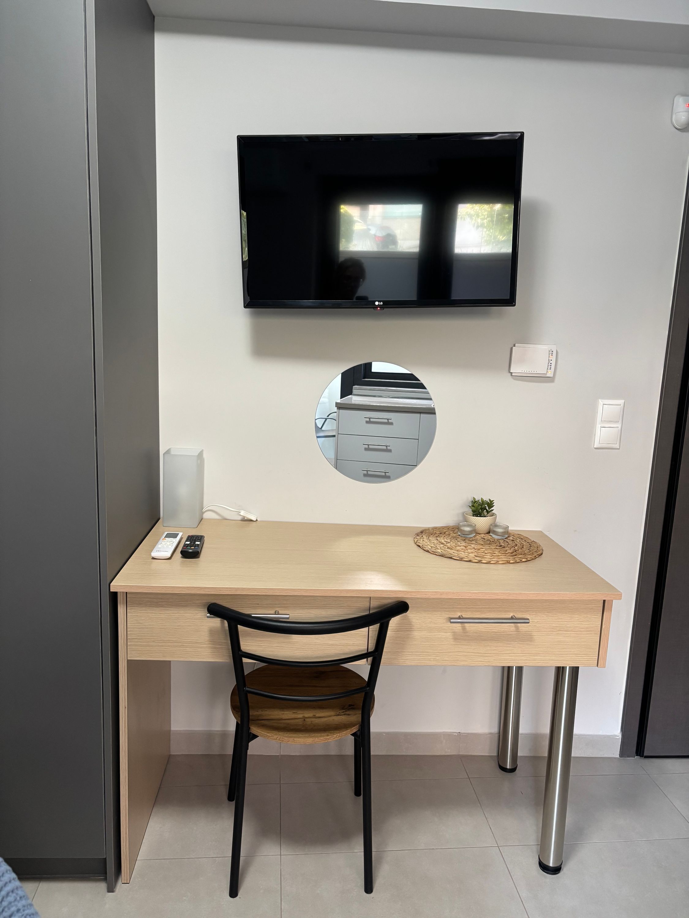 A modern room with a desk, chair, mounted TV, and a small mirror.