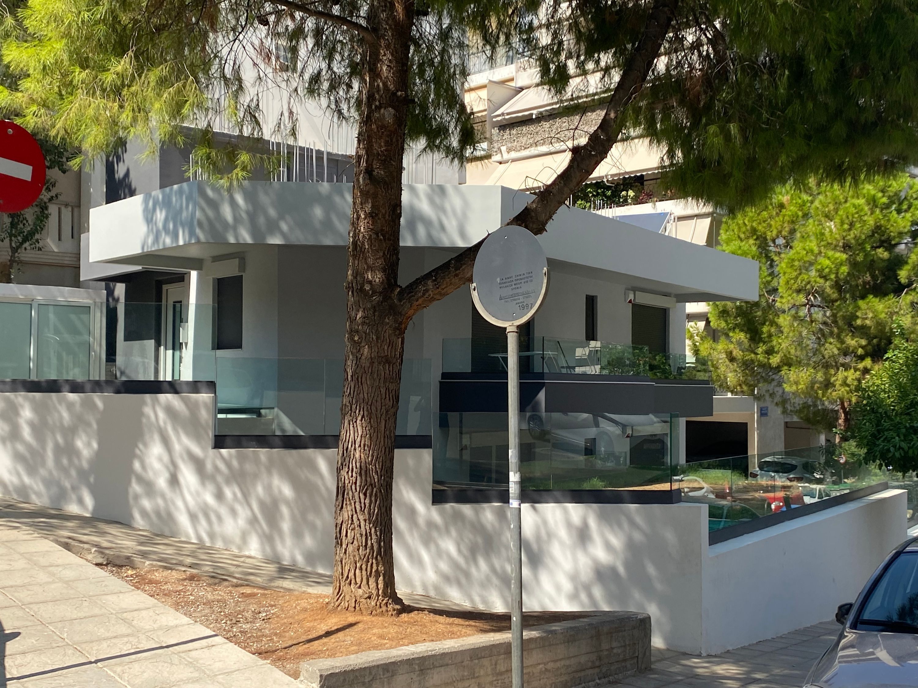 A modern building with a tree in front, a no-entry sign, and a plaque on a pole.