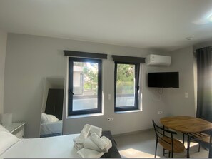 A hotel room with a bed, two windows, a flat-screen TV, and a wooden table. - Feels Like Home (Galatsi)