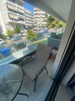 Varanda com cadeira e mesa, com vista para uma rua com carros estacionados e edifícios.
