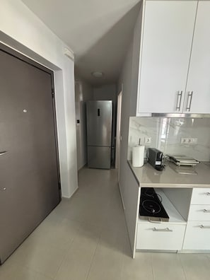 A modern kitchen with white cabinets, a stainless steel refrigerator, a coffee maker, and a countertop with a laptop.