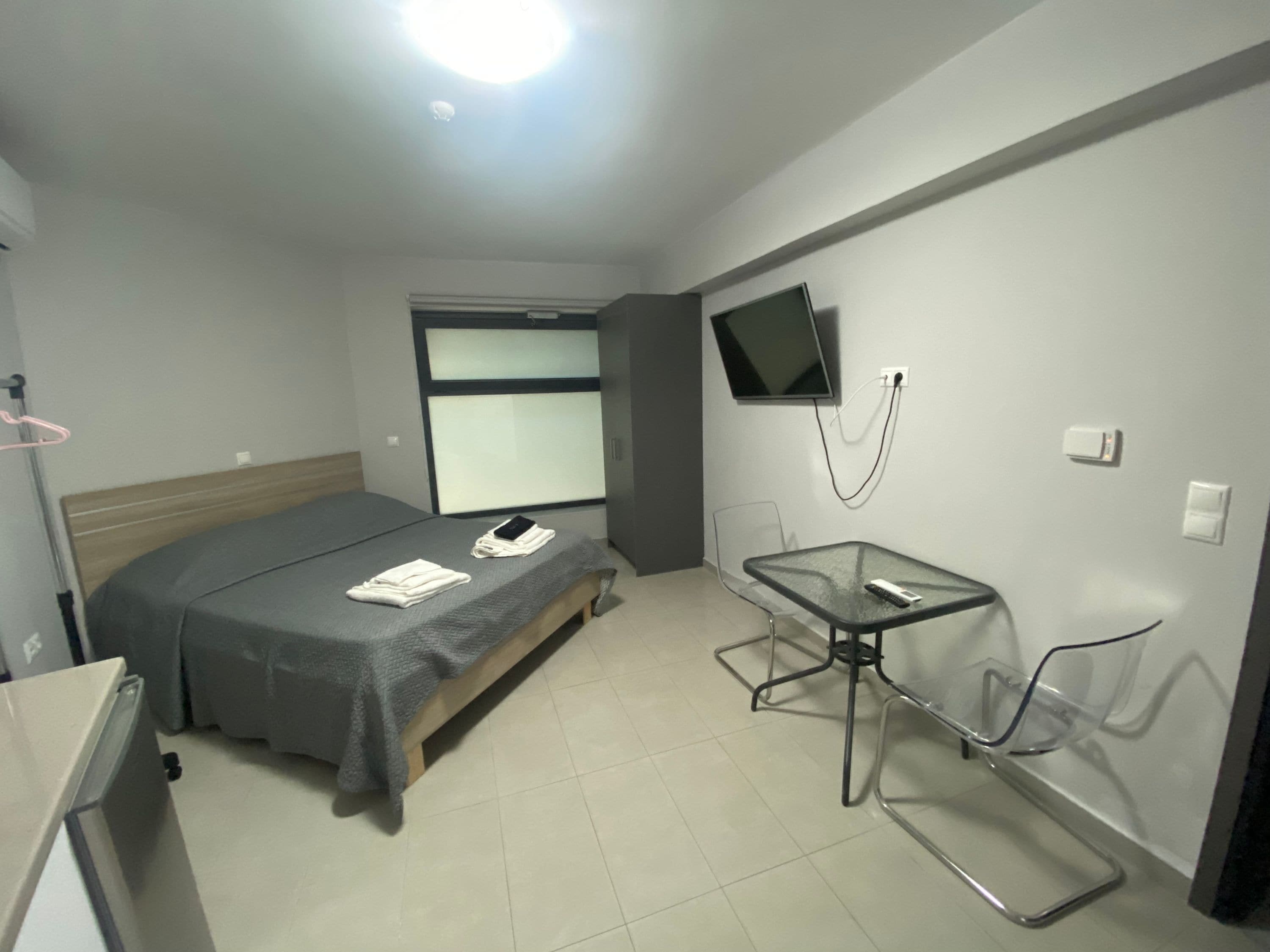 A modern hotel room with a bed, a TV mounted on the wall, a small table, and a chair.