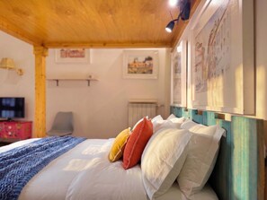 Ein Schlafzimmer mit Holzbalkendecke, einem Bett mit weiß-orangenen Kissen, einer blauen Decke und einem Fernseher auf einem Schrank.