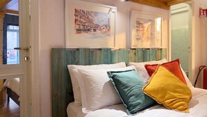A bed with white bedding and colorful pillows, a wooden headboard, and two framed artworks on the wall. - Studio Old Rome - Lungotevere (Rome)
