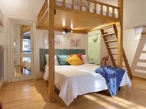 Ein Schlafzimmer mit Etagenbett, einer Holzleiter, einem weißen Bett mit bunten Kissen, einem grünen Kopfteil und einem gerahmten Bild an der Wand.