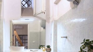 A bathroom with a toilet, sink, mirror, and a small plant. - Studio Old Rome - Lungotevere (Rome)