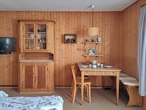 A wooden-paneled room with a television, a cabinet, a dining table with chairs, and a bench. - Chalet Willi-Parterre Appartement/Fewo, Dusche, WC, 2-Bettwohnung by Interhome (Arosa)