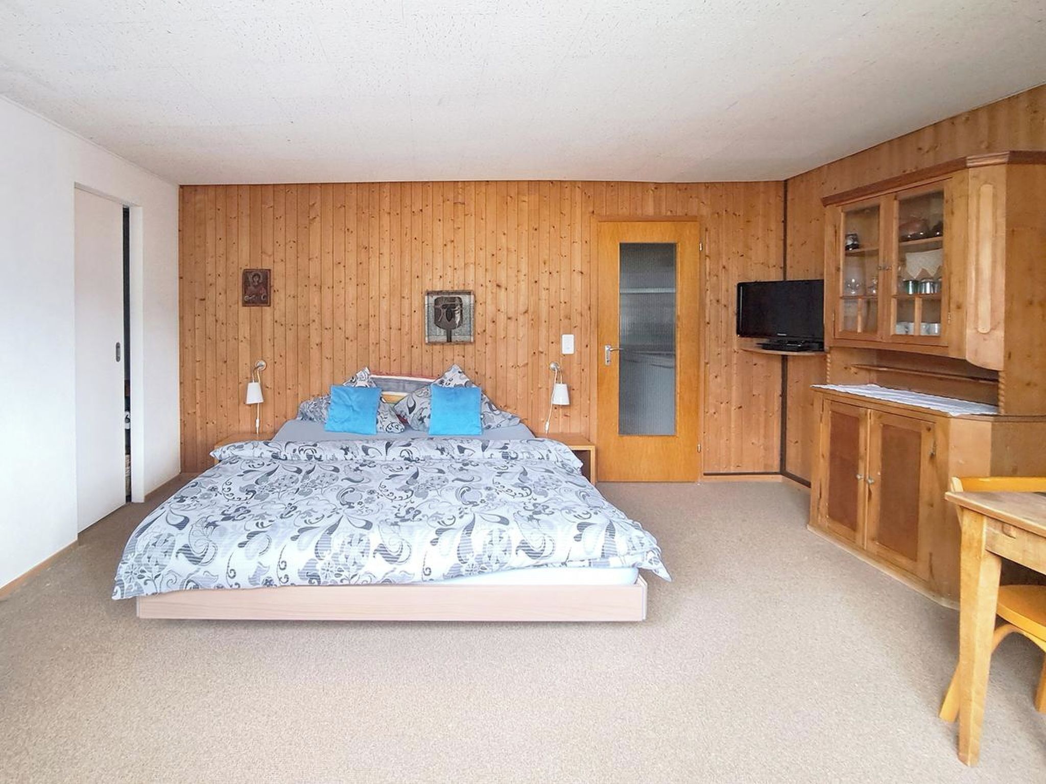 Un dormitorio con cama, paredes de madera, televisor y armario.
