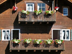 A wooden building with two balconies, each with flower boxes and hanging baskets. - Chalet Willi-Parterre Appartement/Fewo, Dusche, WC, 2-Bettwohnung by Interhome (Arosa)