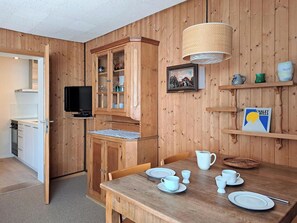 A compact kitchen with wooden cabinets, a television, and a dining table set for four. - Chalet Willi-Parterre Appartement/Fewo, Dusche, WC, 2-Bettwohnung by Interhome (Arosa)