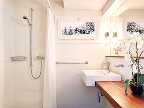 A bathroom with a shower, a sink, and a mirror. There are framed pictures on the wall and a potted orchid on the counter. - Chalet Willi-Parterre Appartement/Fewo, Dusche, WC, 2-Bettwohnung by Interhome (Arosa)