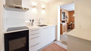 A modern kitchen with white cabinetry, a built-in oven, a stainless steel range hood, and a sink. - Chalet Willi-Parterre Appartement/Fewo, Dusche, WC, 2-Bettwohnung by Interhome (Arosa)